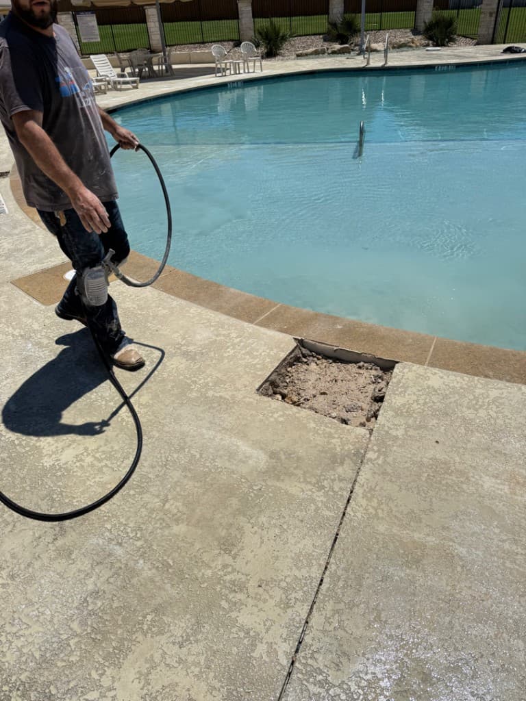 Technician reaching into excavated deck opening to repair pool plumbing — Georgetown